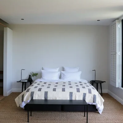 Contemporary bedroom with double bed and crisp white linen decorated with a simple striped throw, two black side tables and an ensuite bathroom. Pine beach.