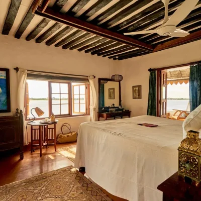 Peponi Hotel bedroom suite with white linen bed looking on to the ocean, wooden cabinets that compliment the beige walls and wooden beam ceilings.