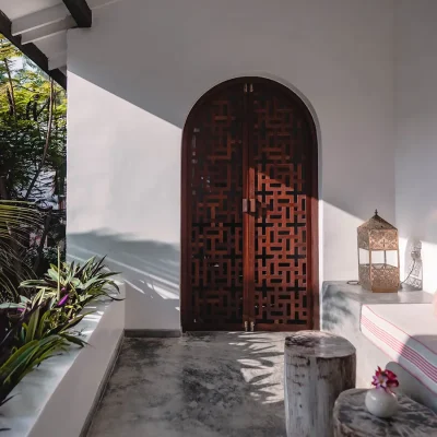 Arched wooden double doors that open onto the verandah with screed floors, white washed walls and a built in sofa with pink and white scatter pillows that looks out onto the Fort garden.