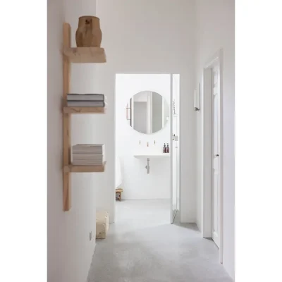 Entrance hall with floating wooden bookshelves facing a bathroom with a single ceramic washbasin and round mirror. Casa Piana.