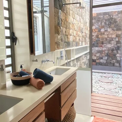 Modern en-suite bathroom with built-in twin sinks and wall mirrors that opens onto a private outdoor stonewall shower.