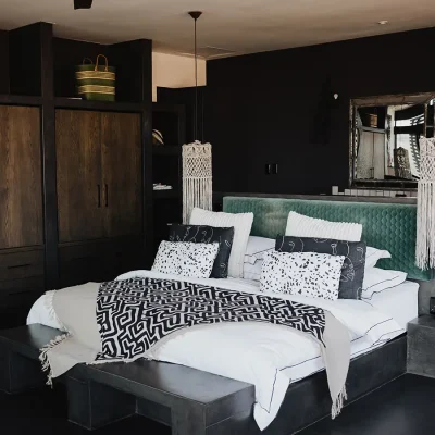 Bedroom suite in the Blogck with a central spacious white linen bed and soft turquoise headboard positioned against charcoal grey walls with large built-in wooden cupboards.