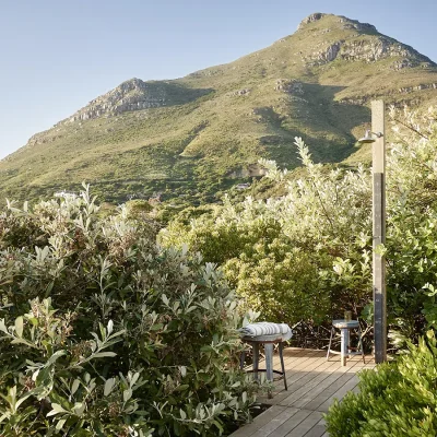 Outdoor shower with a wooden deck surrounded by indigenous vegetation and a backdrop of Chapmans Peak mountain.