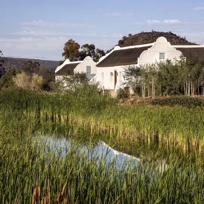 Meandering river populated by reeds, and Buffelsdrift main house with whitewashed walls and a thatch roof in the background.