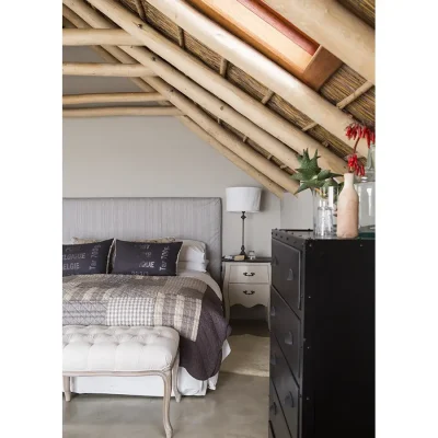 Double bed with crisp white linen and colourful quilt, a beige wooden side table and a black set of drawers positioned between an angled thatch roof. Beach House Zonnestraal.