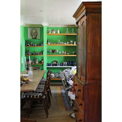 Dining area in Villa Toscana with green walls, and furnished with lengthy wooden table and chairs, an antique mahogany cabinet and wooden floating shelves with glasses.