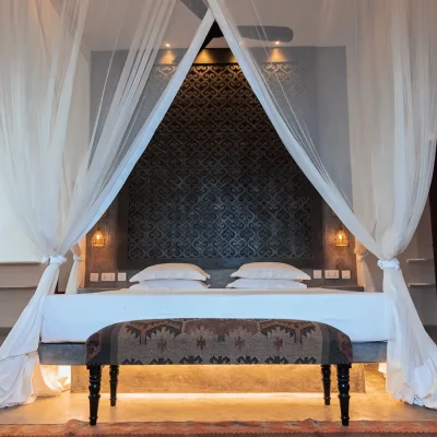 Luxurious bed with crisp white linen and white linen curtains draped around the bed with a large decorative headboard. The Fort bedroom suite.