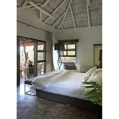 Manor House bedroom suite with white linen folded back on a spacious bad overlooking double doors that open onto a patio with wicker chairs.