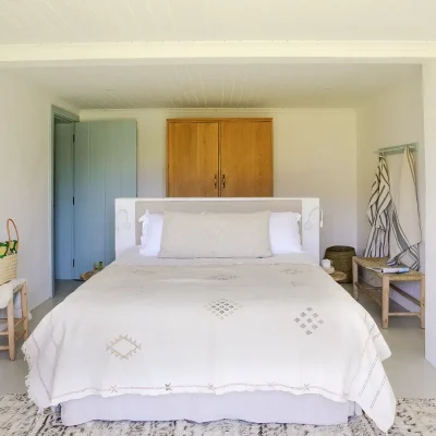 Spacious bed with beige linen bedding that match the flooring, a wooden cabinet and blue wooden door.