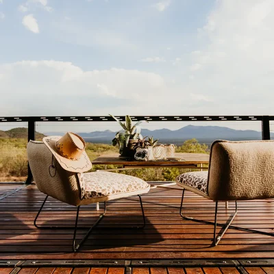 Soft leopard print armchairs and a wooden coffee table on the deck with views of the surrounding reserve and mountain range.