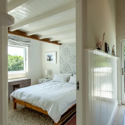 Quaint bedroom in Pebbles home with a fluffy carpet, a double bed with crisp white linen, a floral headboard and glass windows looking out onto the garden.