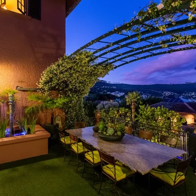 Outdoor garden dining area with large table and chairs, greenery and arching vines overlooking city views. House Nouveau.