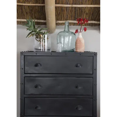 Black metallic drawers with decorative ornaments set against a beige wall and angled thatched ceiling.