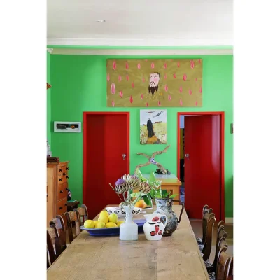 Wooden dining table in Villa Toscana facing a bright green wall with two red doors and wall art.