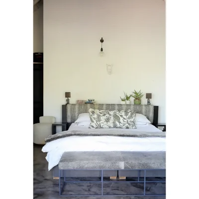 White linen on a double bed with a snake print headboard and grey ottoman at the foot of the bed. Manor house.