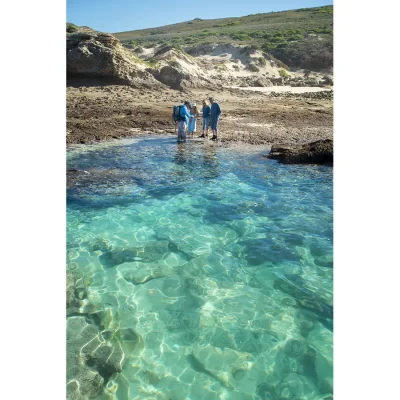 People standing around De Hoop nature reserve rock pools surrounded by crystal clear turquoise water and rugged landscape.