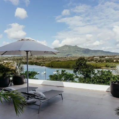 Terrace with sun loungers and a white umbrella for shade overlooks the Black River estuary and mountain range.