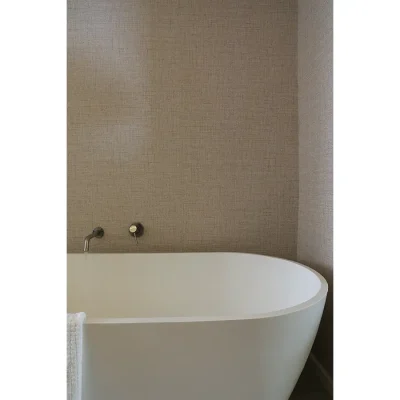 Modern freestanding, bath tub in front of a brown textured wall with simple, bronze taps.