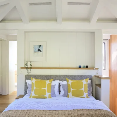 Contemporary bedroom with light hues reflecting in the spacious white linen bed decorated with yellow pillows and positioned against white cladded walls.