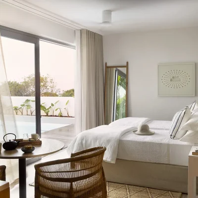 Two joint single beds with white waffle linen, wooden side tables and a small wooden table and wicker chairs that opens onto Walkers Beach Villa pool area.