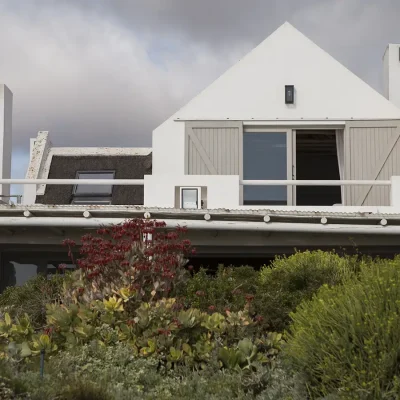 Luscious coastal vegetation in front of Beach House Zonnestraal with whitewashed walls, a thatched roof and beige shutters.