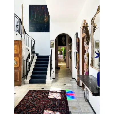 Entrance hallway of Villa Toscana with white marble flooring, a spiral staircase with blue carpets and an arched passage doorway.