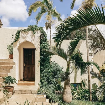 Peponi Hotel courtyard with beige washed walls and arches draped in ivory and surrounded by palm trees and pot plants.