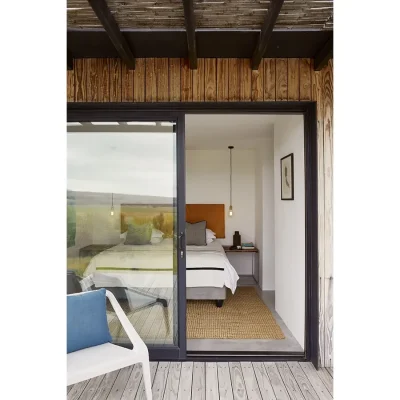 Bedroom with a flood of natural light from the glass sliding doors, furnished with a spacious white bed and burnt orange headboard, two side tables and a white finish.