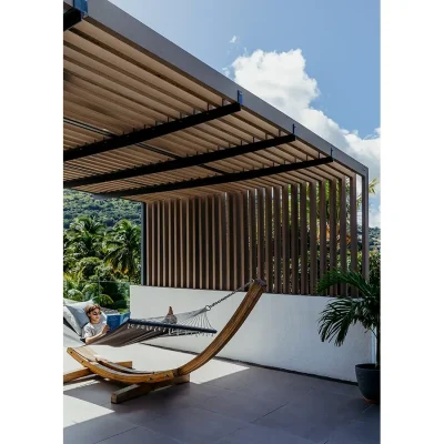 A boy reading a book in a hammock on Black River Penthouse Terrace that is shaded by a wooden pergola.