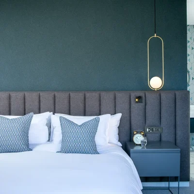 Bedroom suite with a white linen bed and grey velvet headboard mounted against a dark turquoise wall with matching side tables and an ensuite bathroom in Labotessa Hotel.