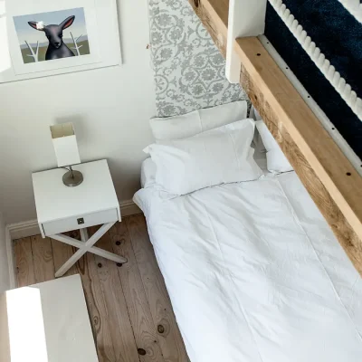 Top view of white doubled bed and simple white wooden bedside table.