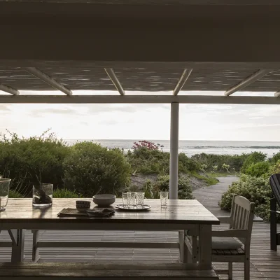 Evening on Beach House Zonnestraal deck with large wooden dining table facing coastal vegetation and ocean views.