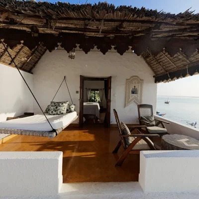 Peponi hotel bedroom suite balcony with a swinging bed and two wicker armchairs that are protected by a thatched roof and overlooking the ocean.