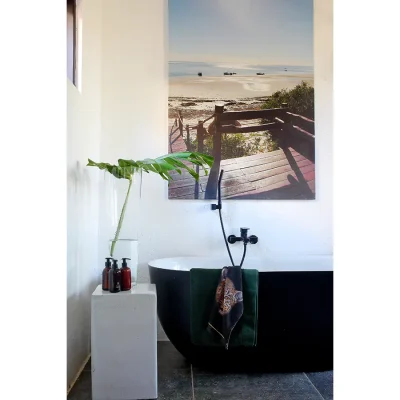 Free standing bath tub with black edging and white inner and a print of the ocean mounted against the whitewashed walls in Manor house bathroom.