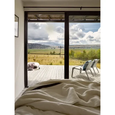 Ruffled beige blanket on bed that opens onto a secluded patio with views of the grassy plains and Maloti mountains from The Herenberg bedroom.