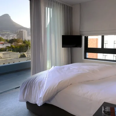 Bedroom suite with luxury white sheets folded back and facing large glass doors that reveal views of Lions Head. Labotessa Hotel.