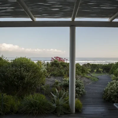 White bamboo pergola with wooden walkway lined with coastal vegetation leading to the ocean front.