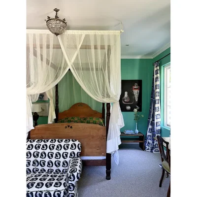 Bedroom with turquoise walls, furnished with a four poster wooden bed draped with mosquito netting, wooden side tables and a black and white sofa at the foot of the bed. Villa Toscana.