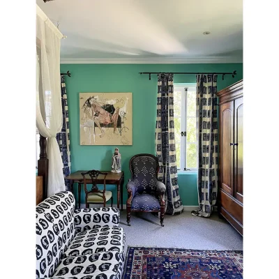 Villa Toscana bedroom suite with turquoise walls, navy armchair, a black and white sofa, and an antique wooden cabinet.