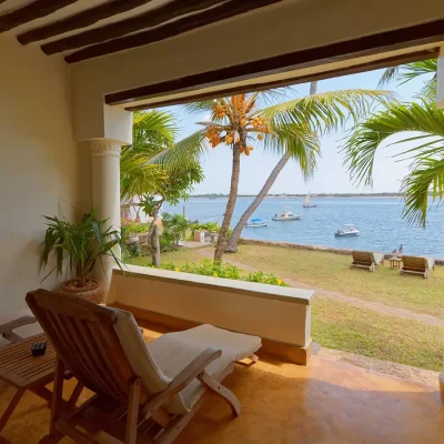 Peponi Hotel bedroom suite patio with wooden sun loungers facing the green lawn and ocean.