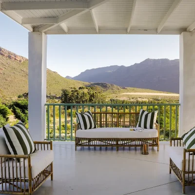 Wrap around verandah at Buchubos Villa with white cushioned wicker sofa and armchairs overlooking the luscious landscape and surrounding mountain range.