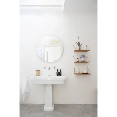 Casa Piana bathroom with white washed walls, ceramic washbasin, rounded mirror and mini wooden floating shelves.