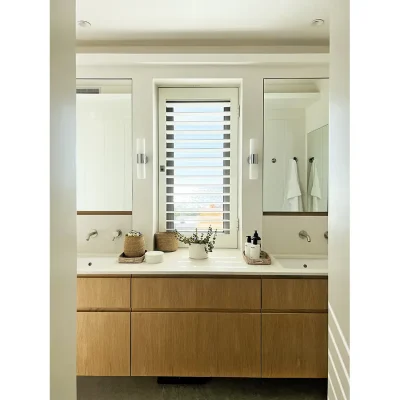 Bathroom with sleek wooden cabinets, white granite tops with built in twin wash basins and mirrors mounted on the wall with a central window.