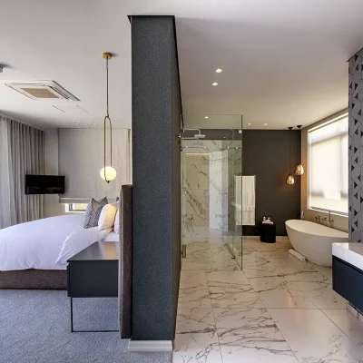 Labotessa Hotel with spacious presidential suite furnished with crisp white linen bed facing large stack back doors that open onto the balcony, and a large bathroom with charcoal walls, marbled floors, a glass enclosed shower and white bath tub with a granite washbasin.