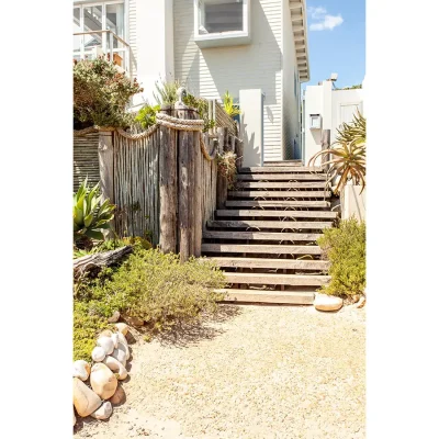 Foot path lined with coastal vegetation leading to a Wooden staircase connected to Pebbles home.