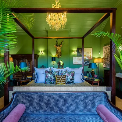 Bright green bedroom with four poster bed, palm trees, hunting trophy and chandelier. House Nouveau.