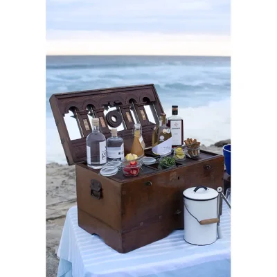 A wooden trunk set on a table on the beach and stocked with picnic goods.