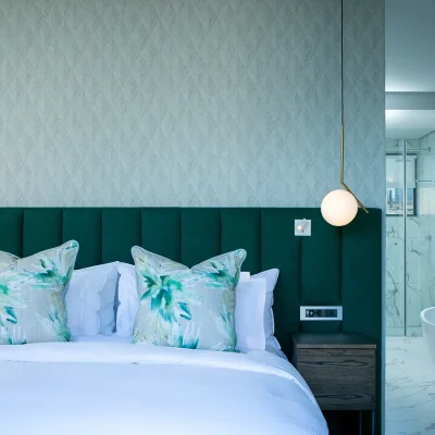 Bedroom suite at Labotessa Hotel with green shades reflective on the mint textured wall, the velvet green headboard and floral scatter pillows perched on the crisp white linen bed, and an adjacent ensuite bathroom with galaxy print walls and large freestanding bath tub.