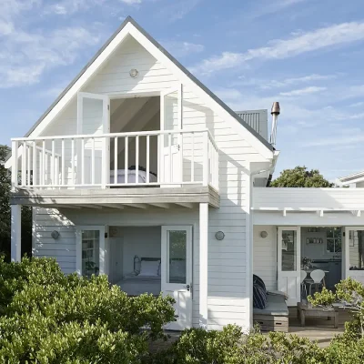 Noordhoek Beach House extension with white cladded walls, a wooden deck with outdoor furniture and bedroom's on the first and second floor with glass double doors.