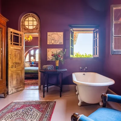 Victorian bath with occasional chair and large wooden mirror wardrobe with natural light pouring in. House Nouveau.